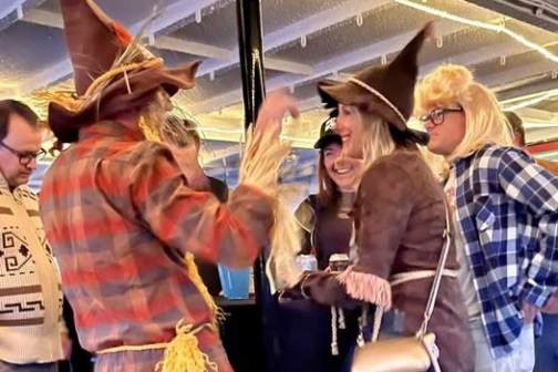 Group in costumes talking, two wearing wizard hats, inside a room with overhead lights.